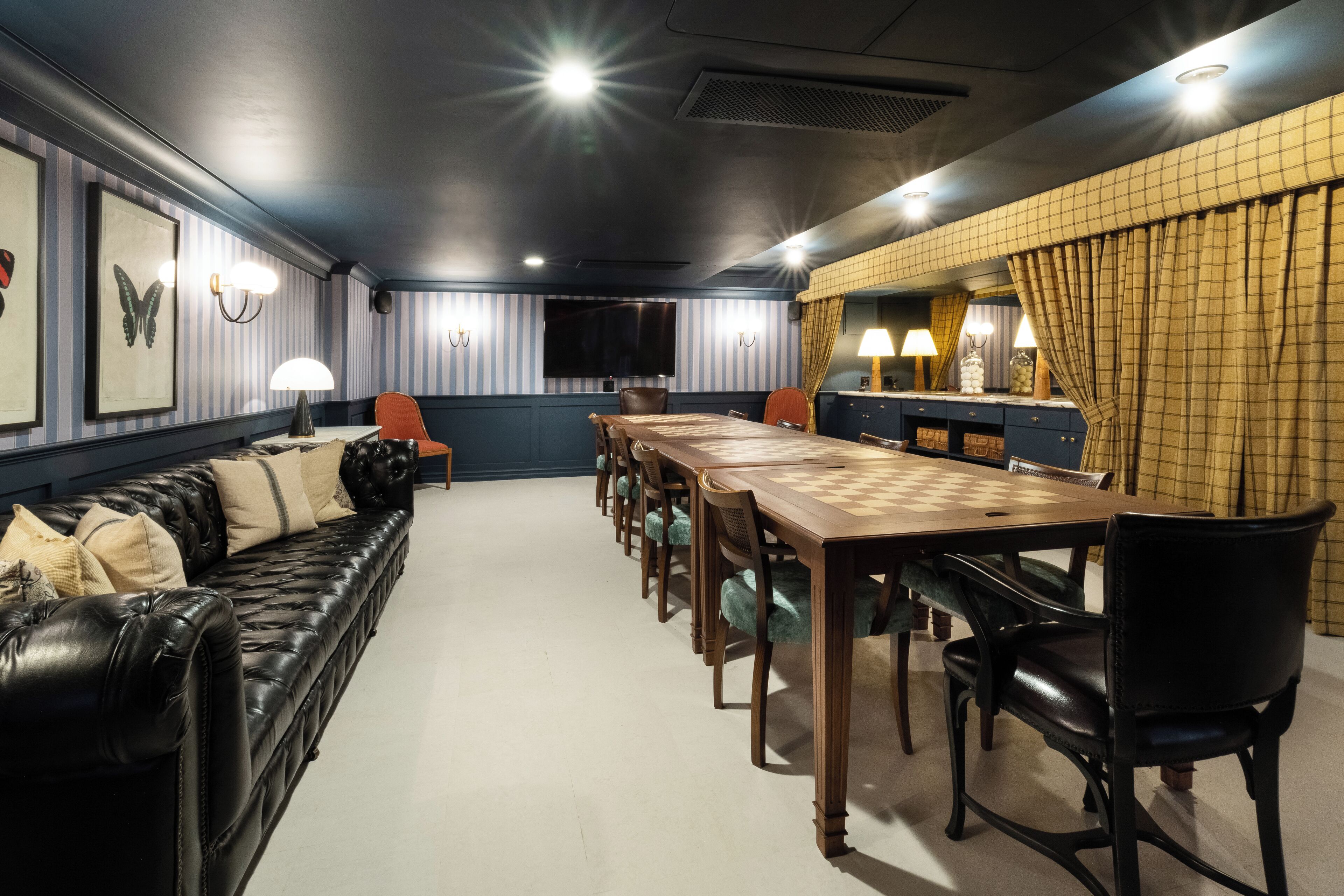 A dining area with a long wooden table, black leather sofa, and a television on the wall.