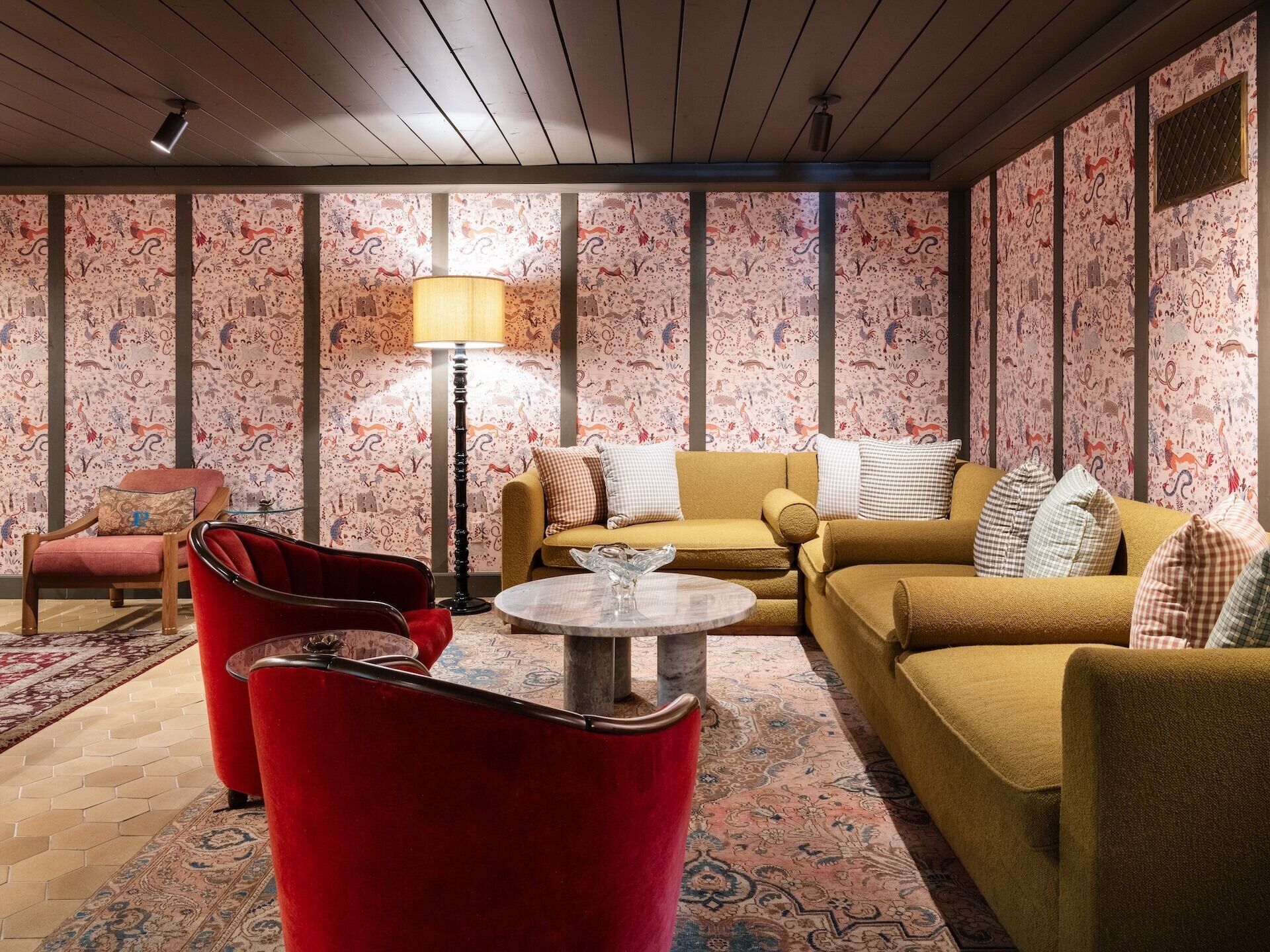 Ein Wohnzimmer mit gemustertem Wandpapier, einem roten Sessel, einem gelben Sofa und einer Stehlampe.