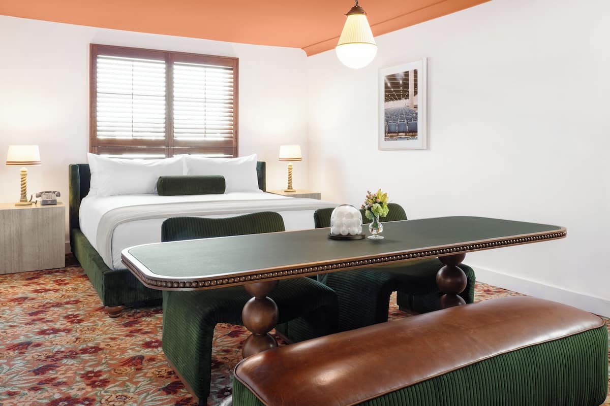 Een hotelkamer met een bed, bedlampen, een tafel met een bloemetjesvaas, en een bankje.