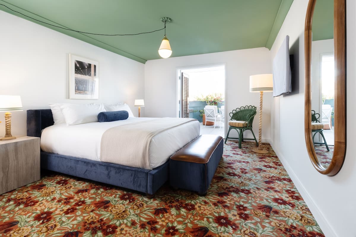 Een slaapkamer met een bed, nachtkastjes, een bankje, een spiegel en uitzicht op het groen.