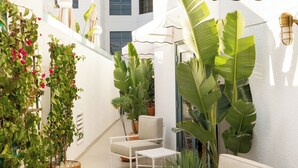 A modern outdoor seating area with white furniture, large potted plants, and a white building in the background.