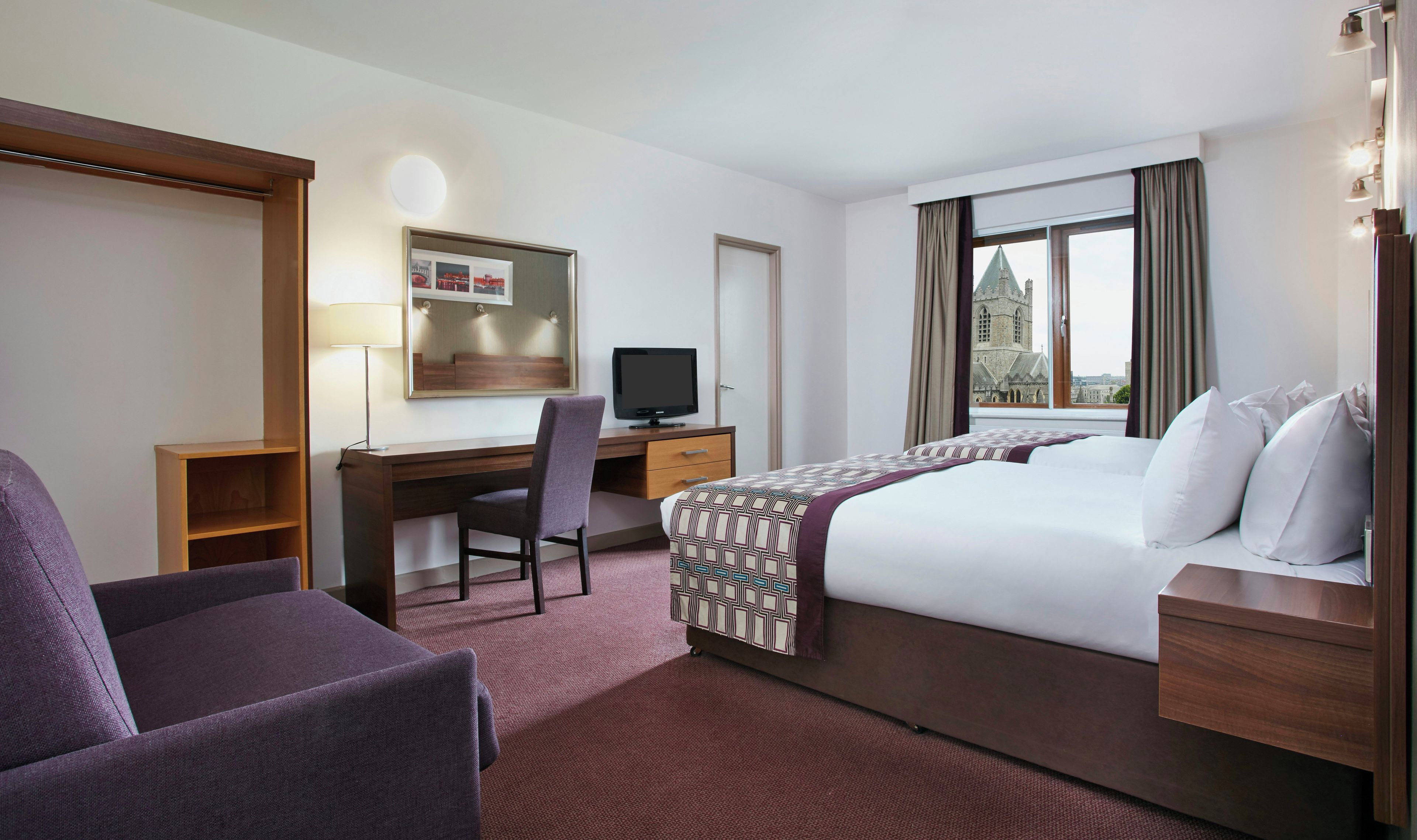 Una habitación de hotel con cama, escritorio con silla, televisión y ventana con cortinas.