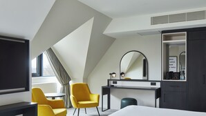 Een hotelkamer met een bed, een bureau, twee gele stoelen, een ronde tafel, een spiegel en een kledingkast.