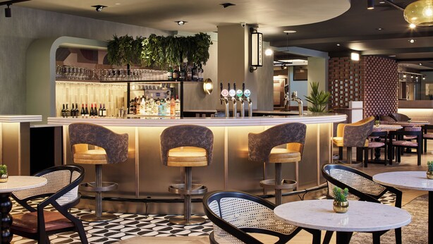 Een bar met zitplaatsen, een toonbank vol flessen en een vloer met patroon.
