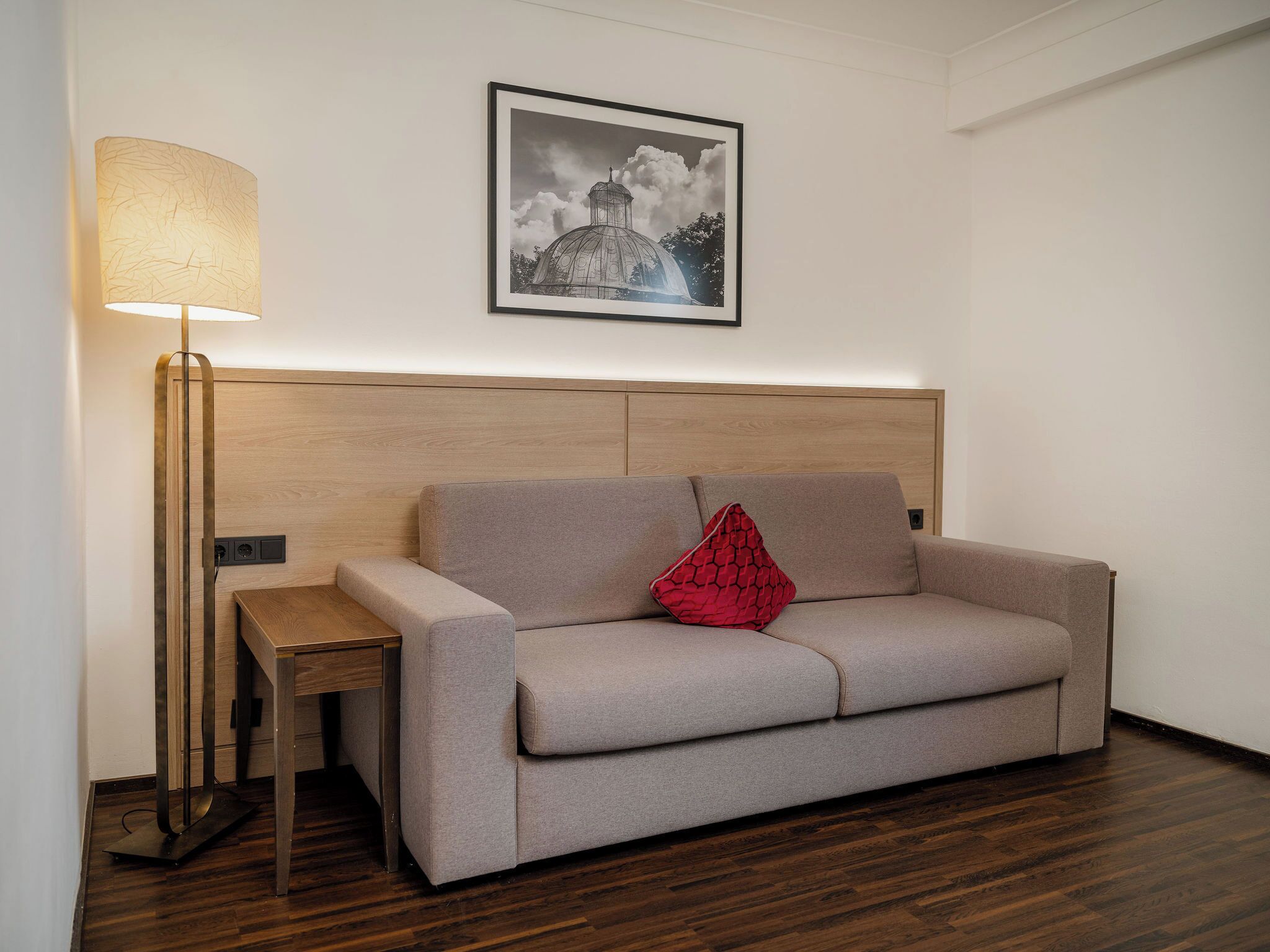 Ein modernes Zimmer mit einer Couch, einem Beistelltisch, einer Stehlampe und einem gerahmten Bild an der Wand.