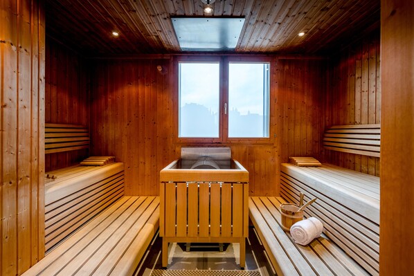 A sauna with wooden benches and a central bench, large windows, and a skylight.