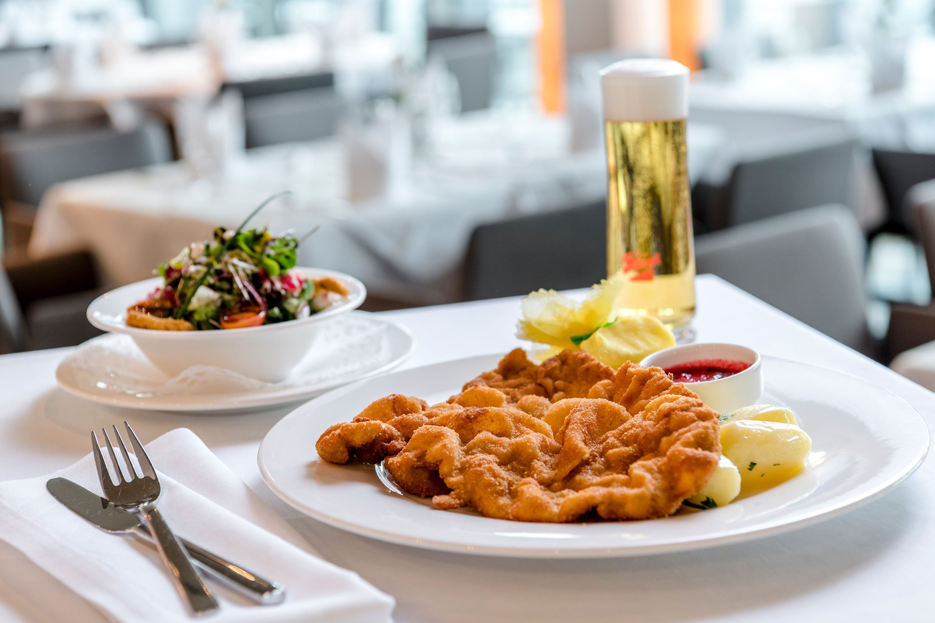A dining table with a plate of schnitzel, boiled potatoes, and a side salad.