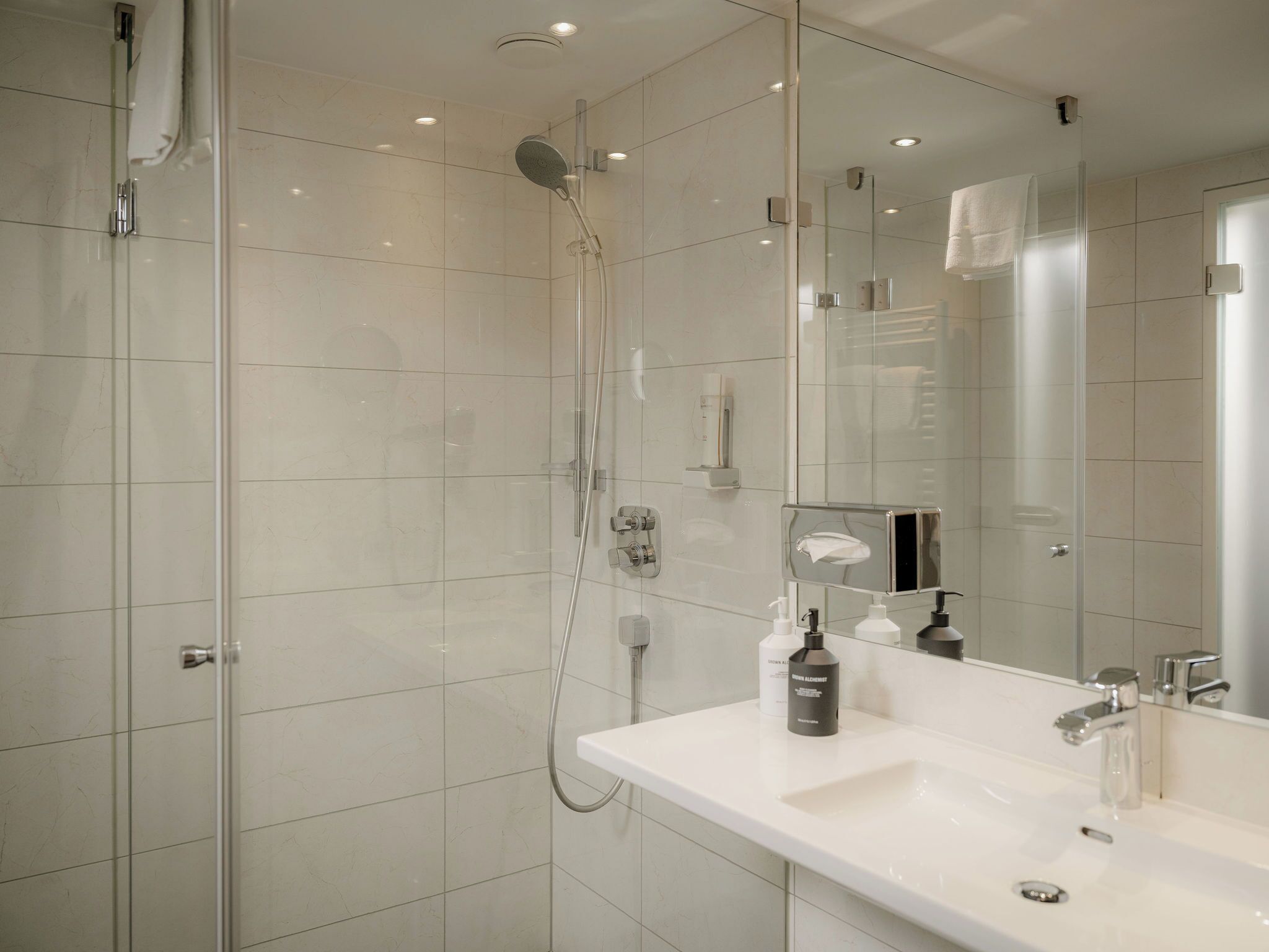 A modern bathroom with a glass shower enclosure, a white sink with a mirror, and a handheld showerhead.