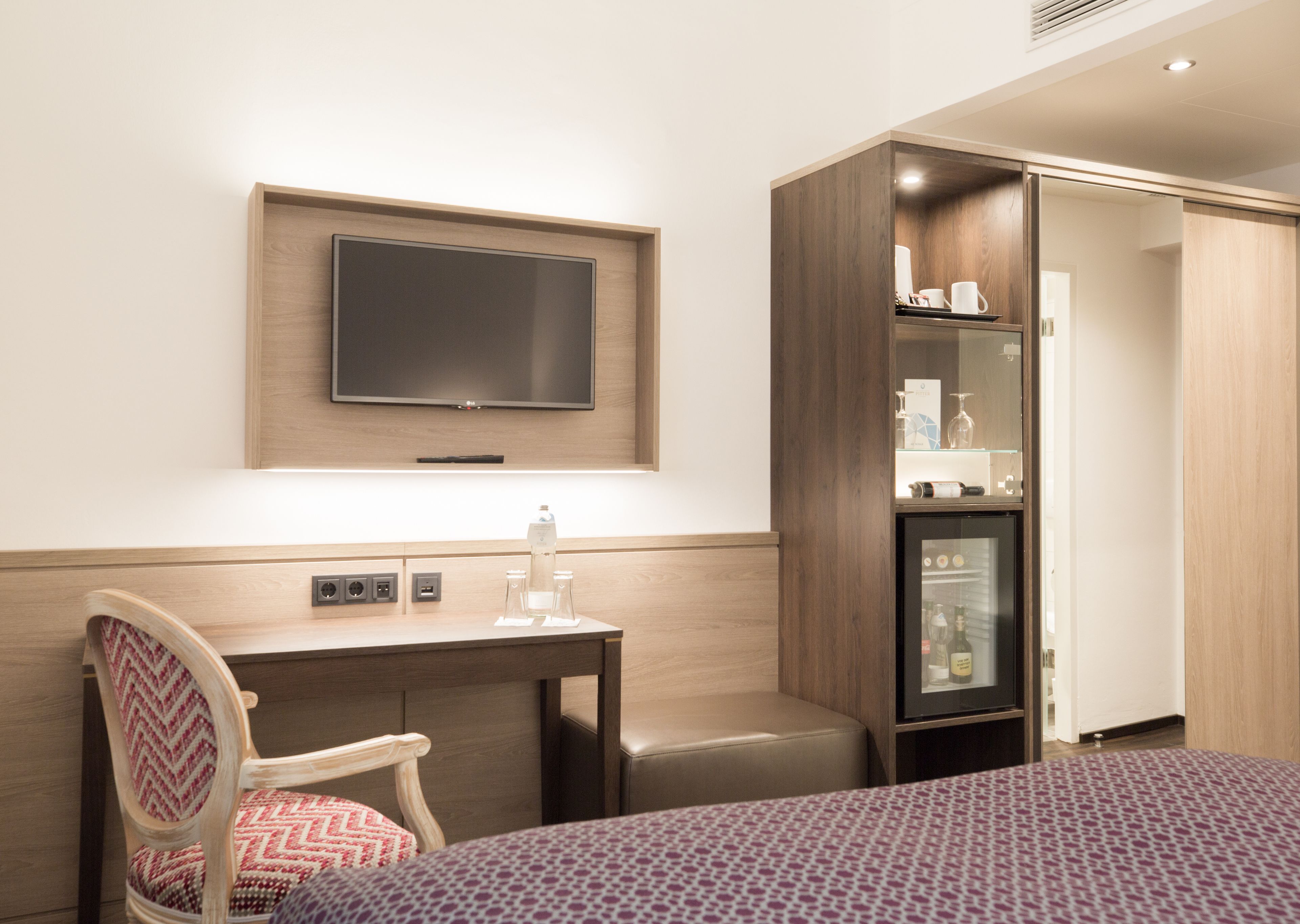 Une chambre d’hôtel comprenant un lit, un bureau avec une chaise, une télévision, un minibar et une armoire.