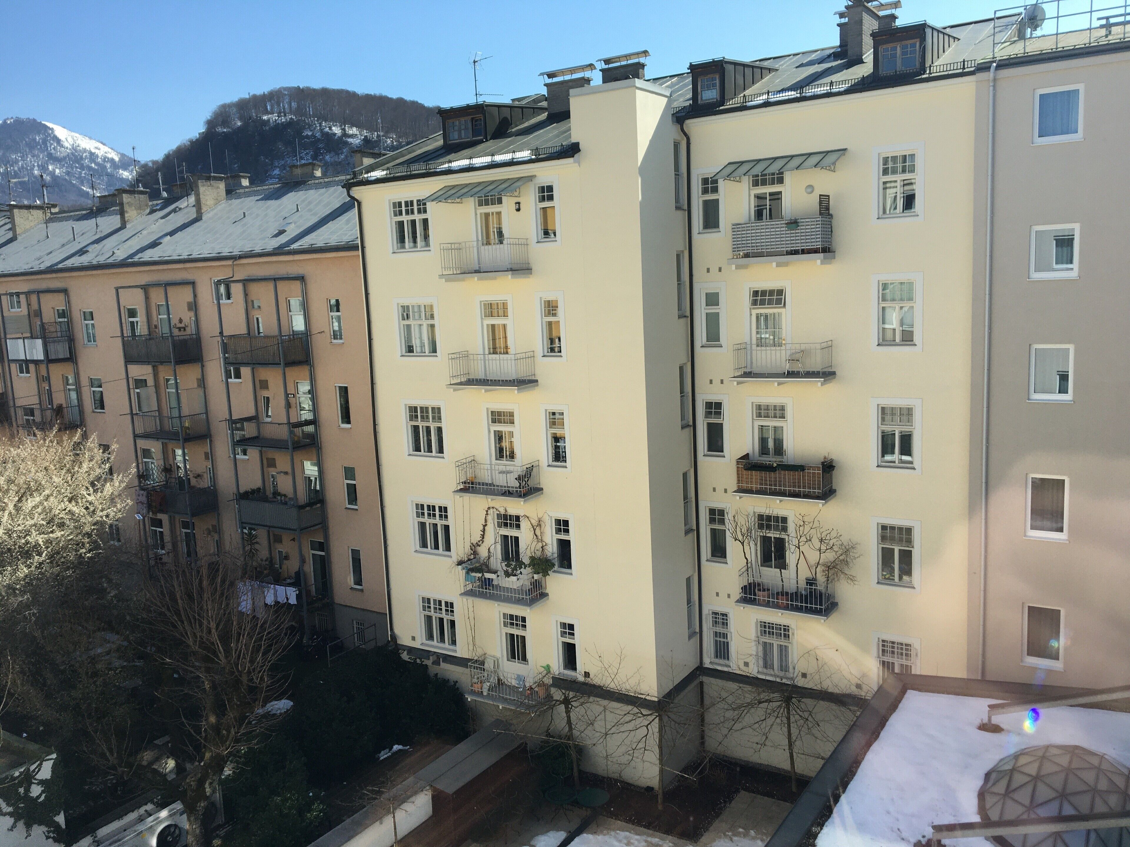 A multi-story residential building with balconies, a snow-covered roof, and a mountain in the background.