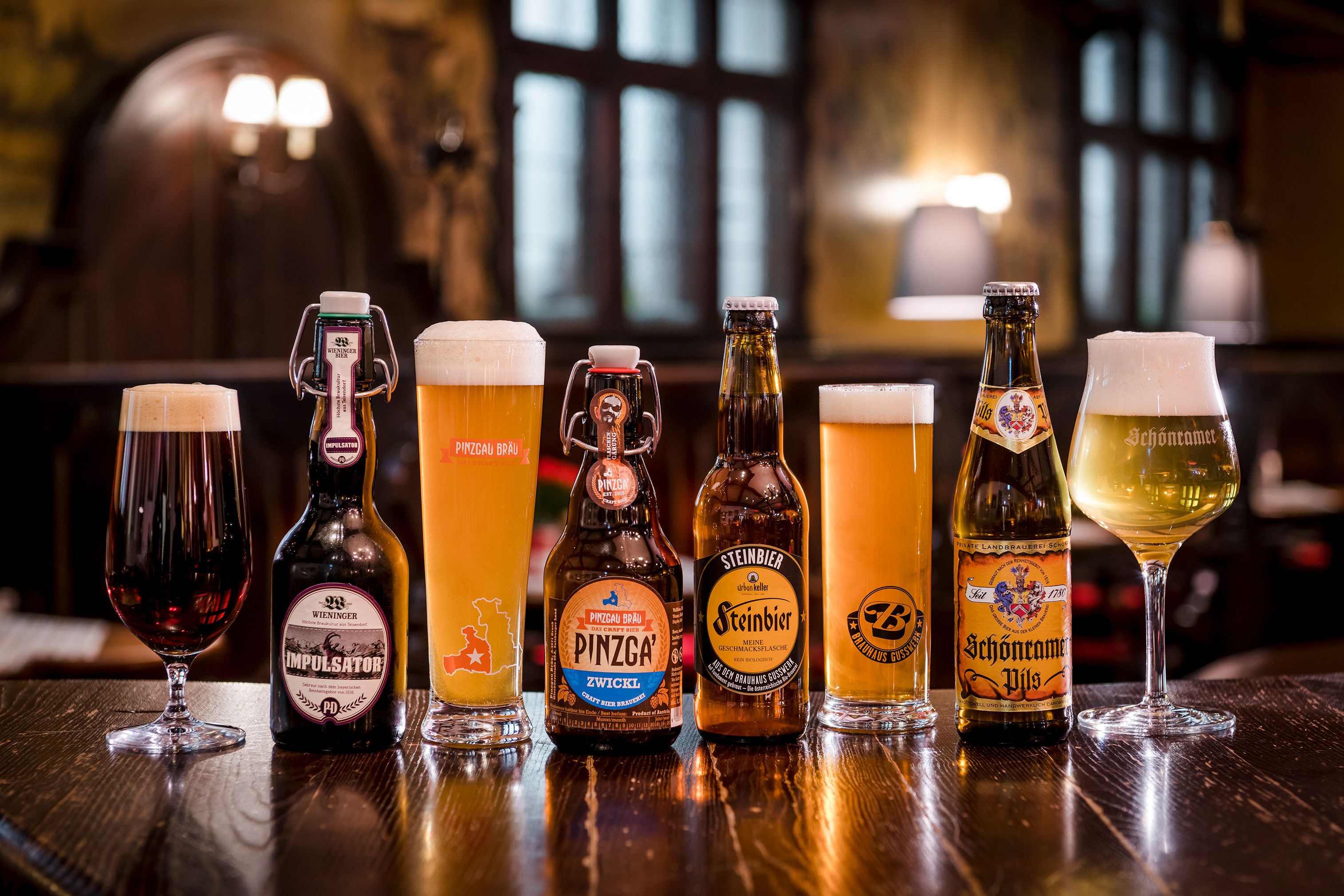 A selection of beer bottles and glasses on a wooden table in a bar setting.