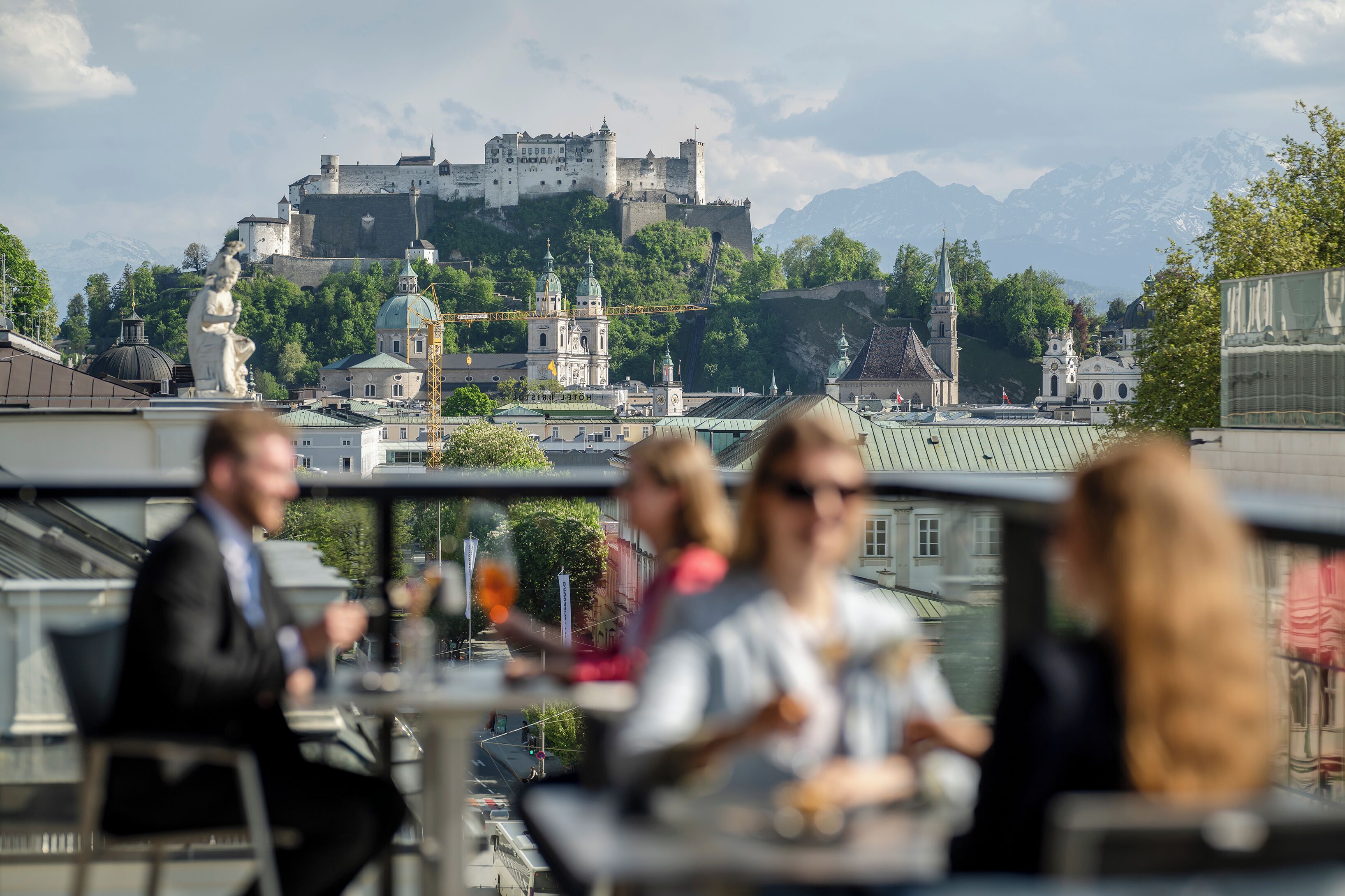 En restaurant med udendørs siddepladser med udsigt over et historisk slot og bjerge.