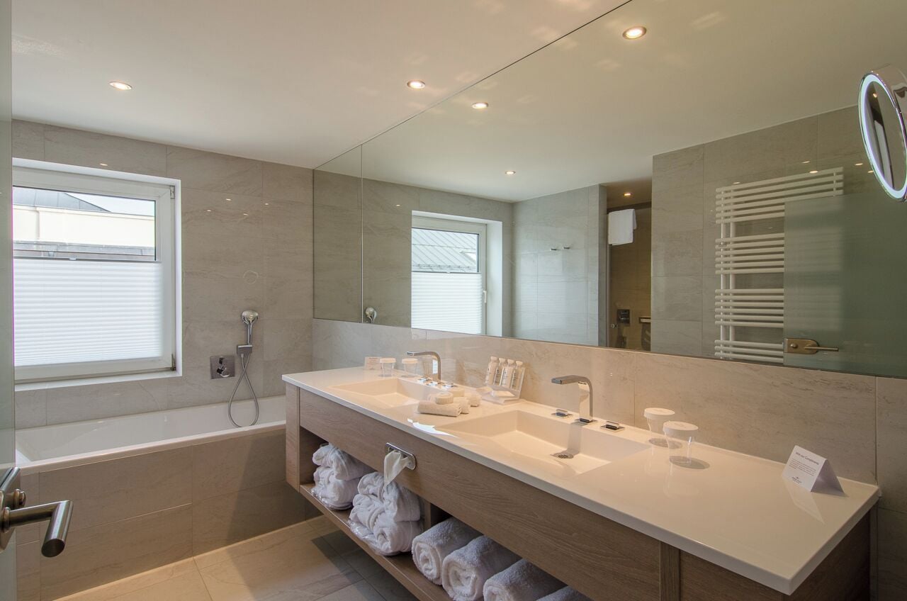 A modern bathroom with a dual sink vanity, a large mirror, a built-in towel rack, and a separate shower area.