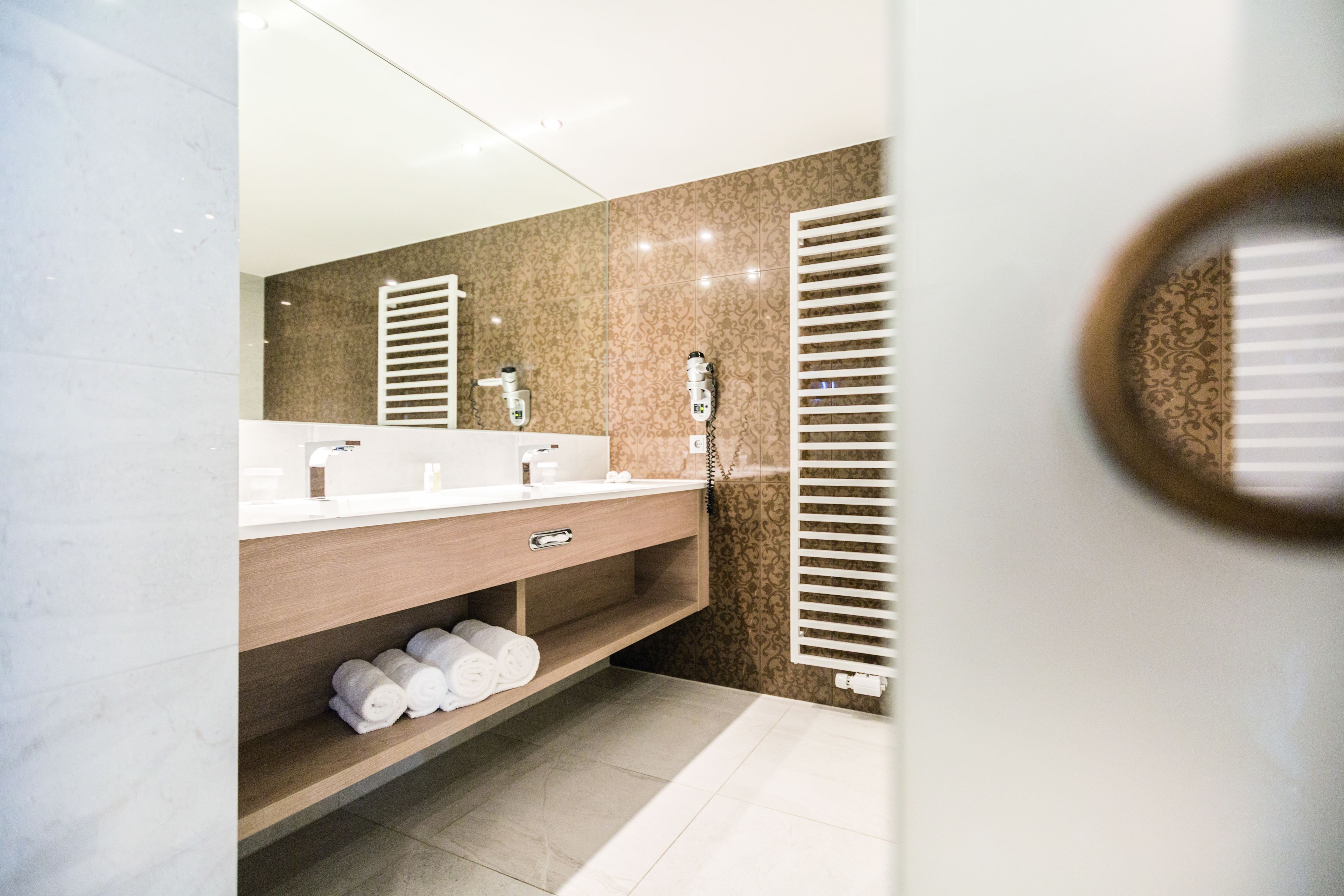 Un baño moderno con un espejo grande, dos lavamanos, un perchero para toallas y una ducha.