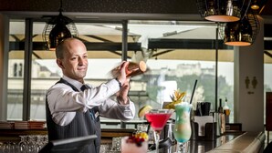 A bartender preparing a drink at a bar with a city view, a variety of cocktail glasses, and a well-organized bar area. - IMLAUER Hotel Pitter Salzburg (Salzburg)