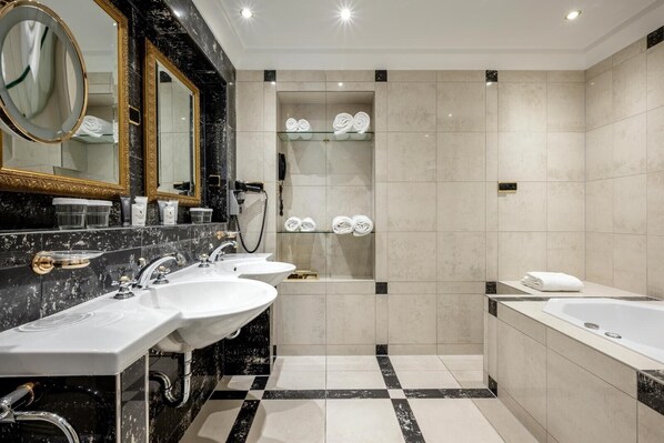 A modern bathroom with three sinks, a large mirror, a shower area, and a bathtub.