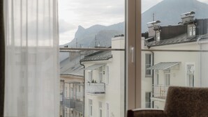 A room with a large window, two sofas, a small round table with vases, and a view of buildings and mountains. - IMLAUER Hotel Pitter Salzburg (Salzburg)