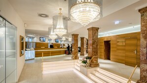 A hotel lobby with a reception desk, large chandeliers, marble columns, and a staircase with illuminated steps. - IMLAUER Hotel Pitter Salzburg (Salzburg)