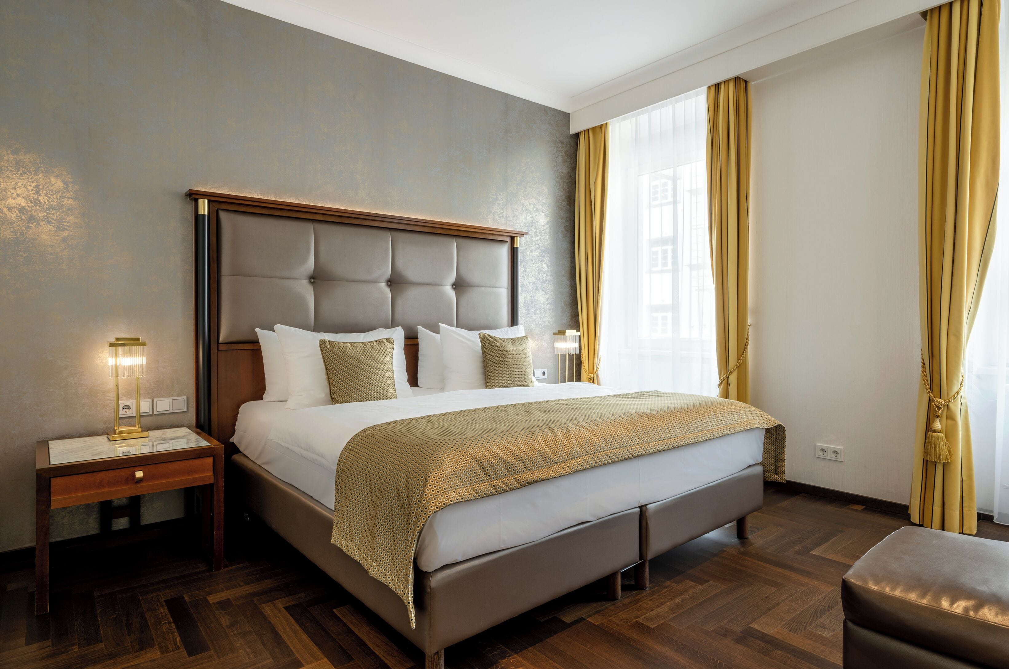 A hotel room with a large bed, a nightstand with a lamp, and a wooden floor.