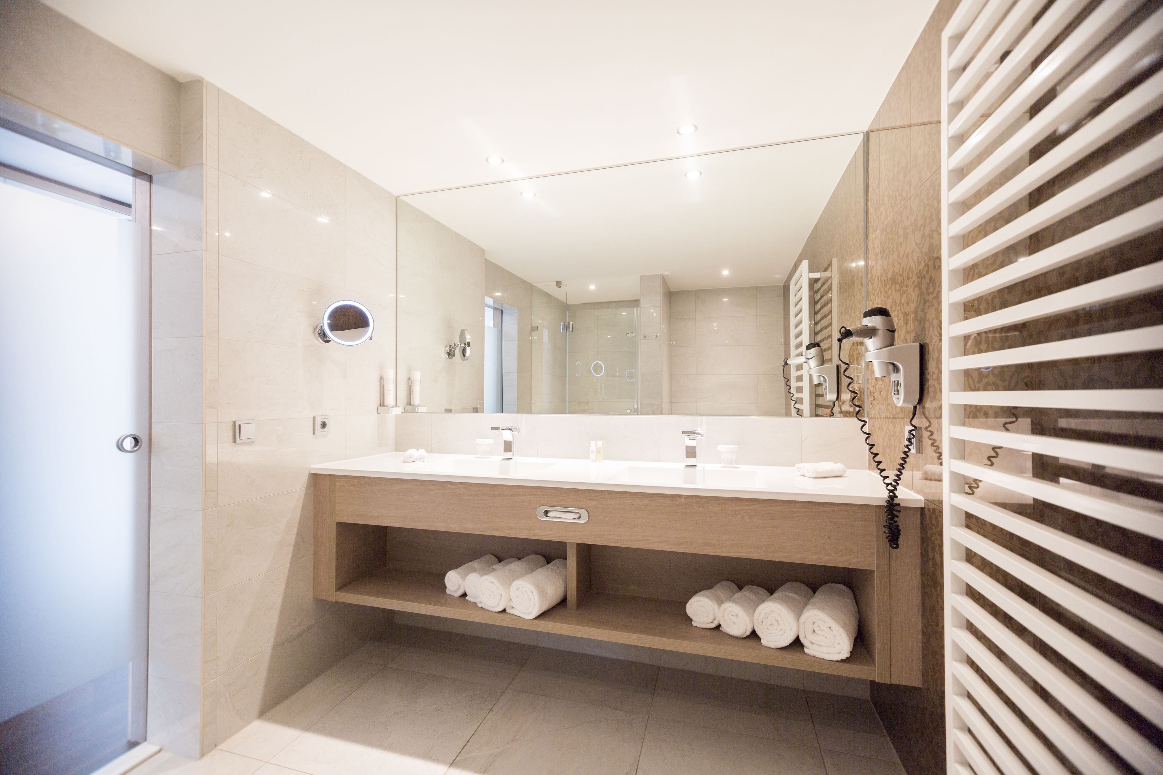 A modern bathroom with a large mirror, two sinks, and a towel rack.
