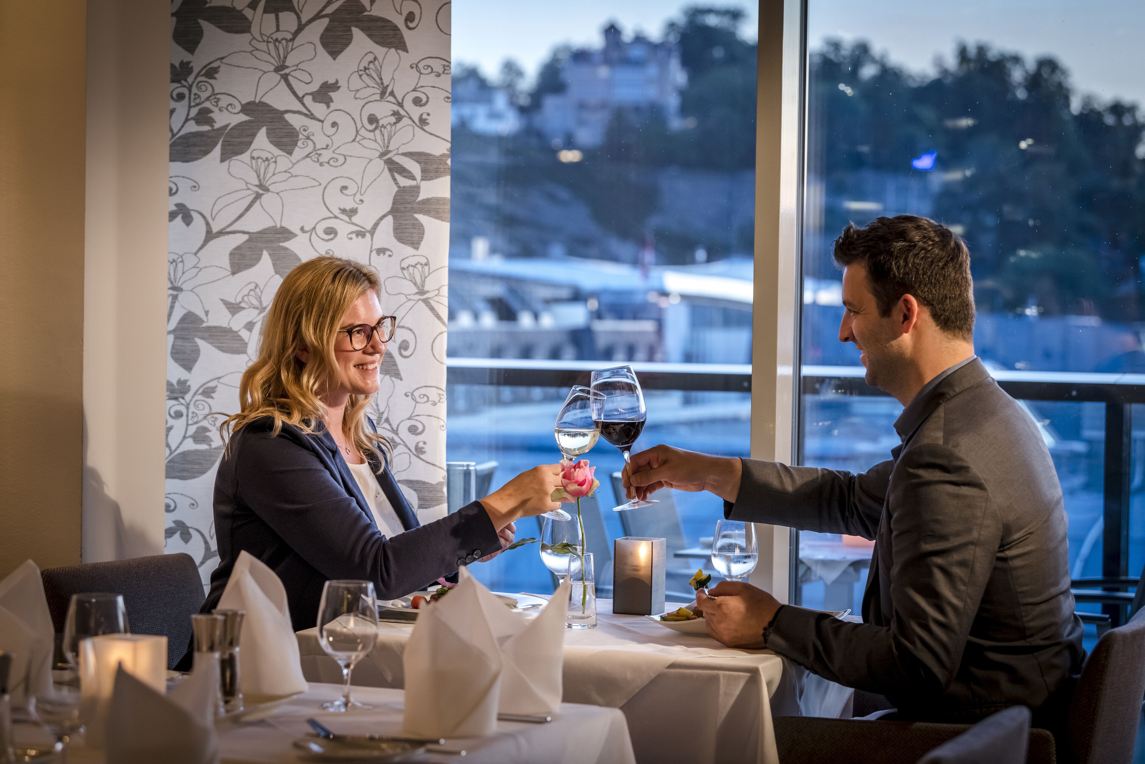 A dining table with wine glasses, a candle, and a vase with a rose.