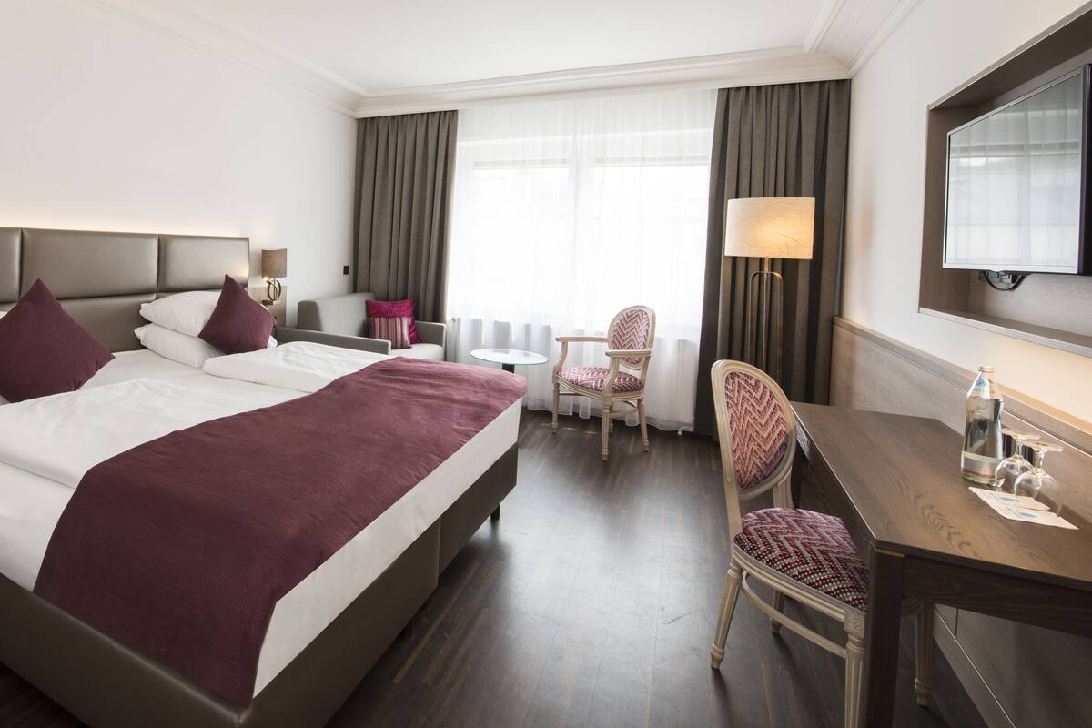 A hotel room with a large bed, bedside tables, a desk, a chair, and a TV.