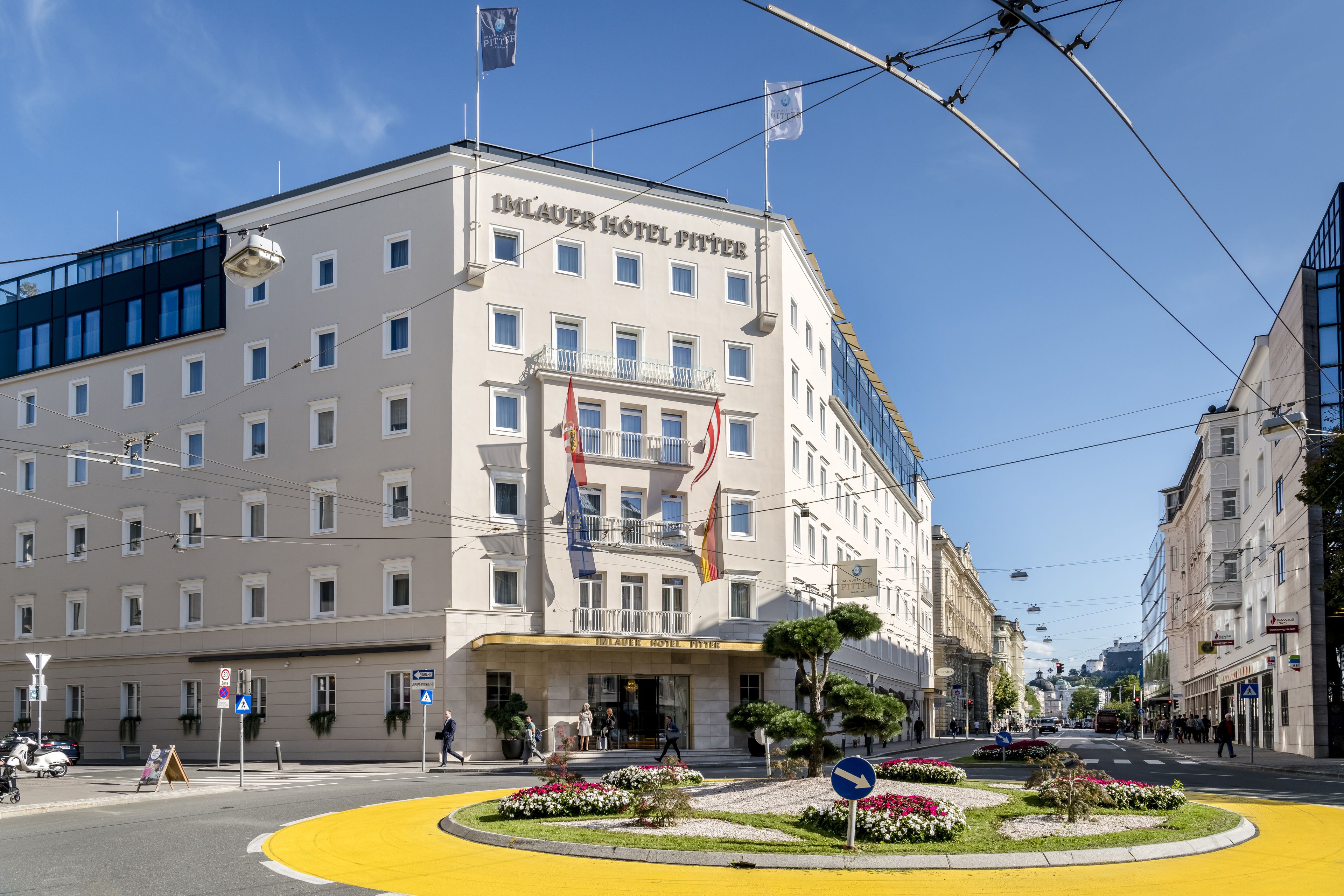 A hotel with a classic facade, multiple windows, and a yellow circular traffic island with flowers.