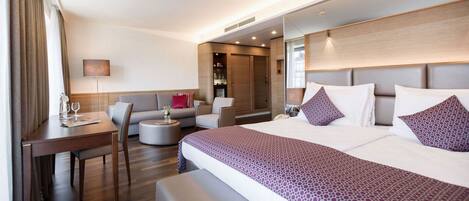 Una habitación de hotel moderna con una cama grande, un escritorio, un sofá y una pequeña zona de estar.