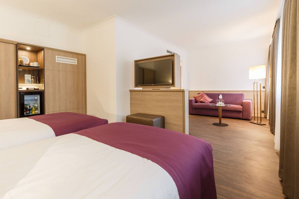 A hotel room with two beds, a sofa, a TV, and a minibar.