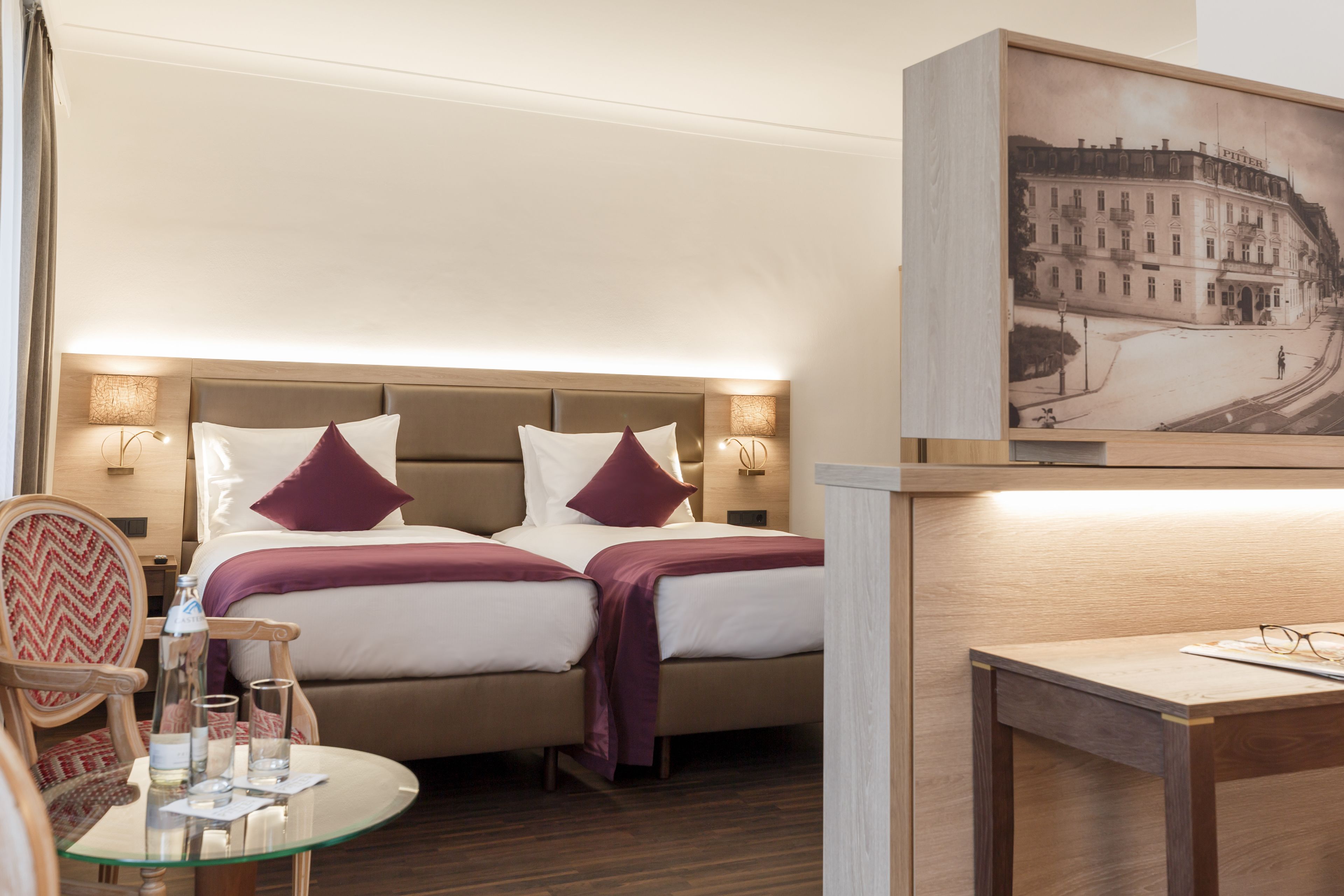 Ein Hotelzimmer mit zwei Betten, einem Glastisch, einem Stuhl und einem Bild an der Wand.