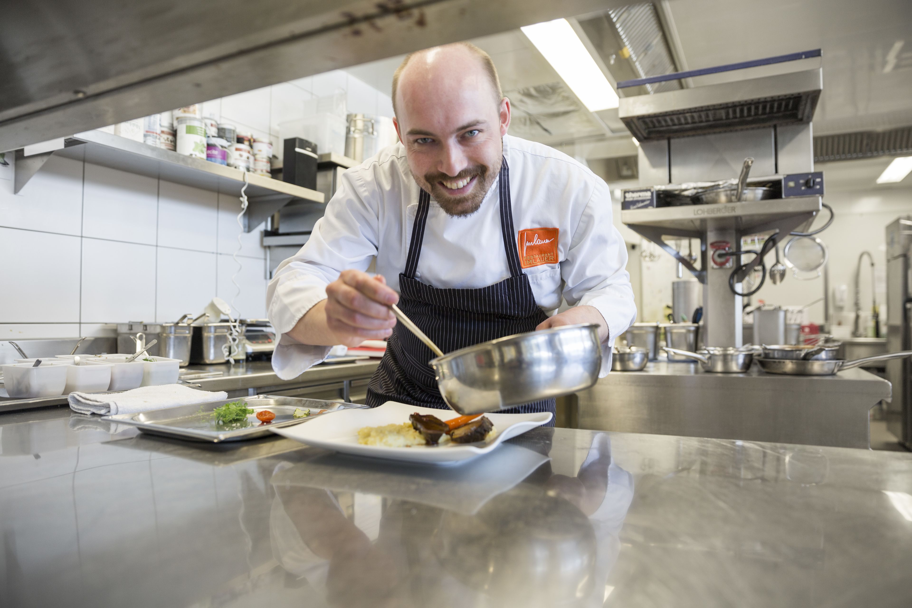A chef in a professional kitchen with stainless steel surfaces, cooking equipment, and a clean, organized layout.