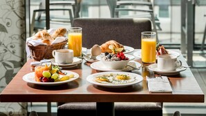 A breakfast table with various dishes, including eggs, toast, and fruit, set against a backdrop of a cityscape and mountains. - IMLAUER Hotel Pitter Salzburg (Salzburg)
