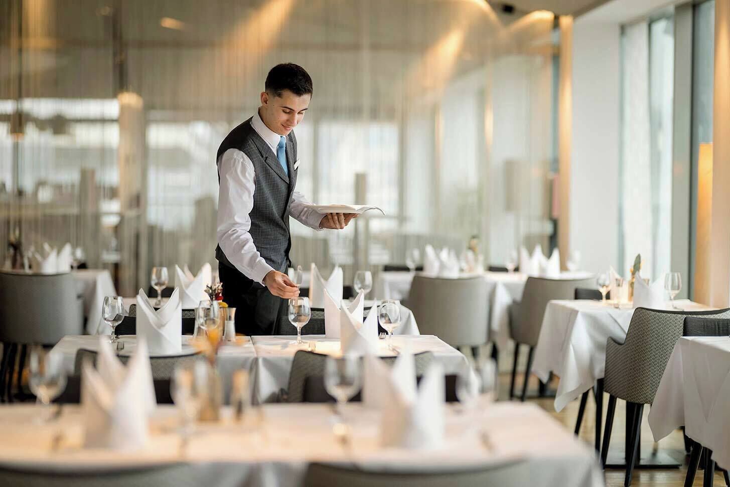 A restaurant with tables set for dining, a waiter serving, and a modern interior.