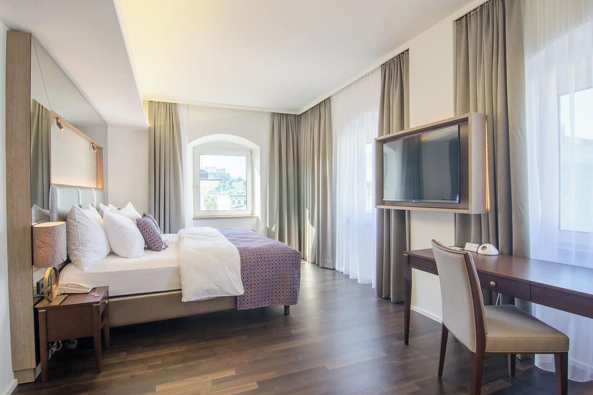A hotel room with a bed, a desk, a TV, and a window with curtains.