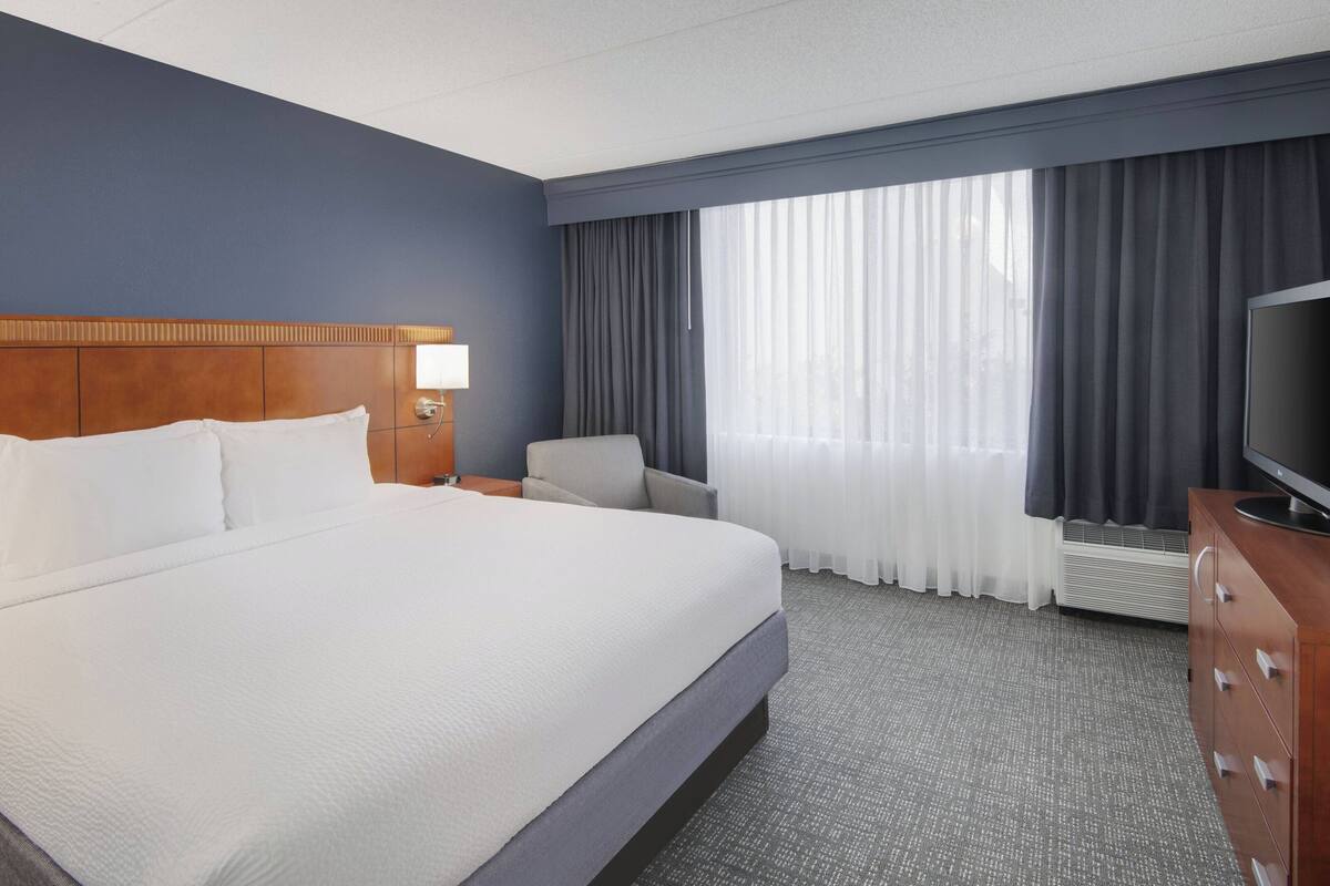 A hotel room with a large bed, a desk, a chair, a TV, and a window with curtains.