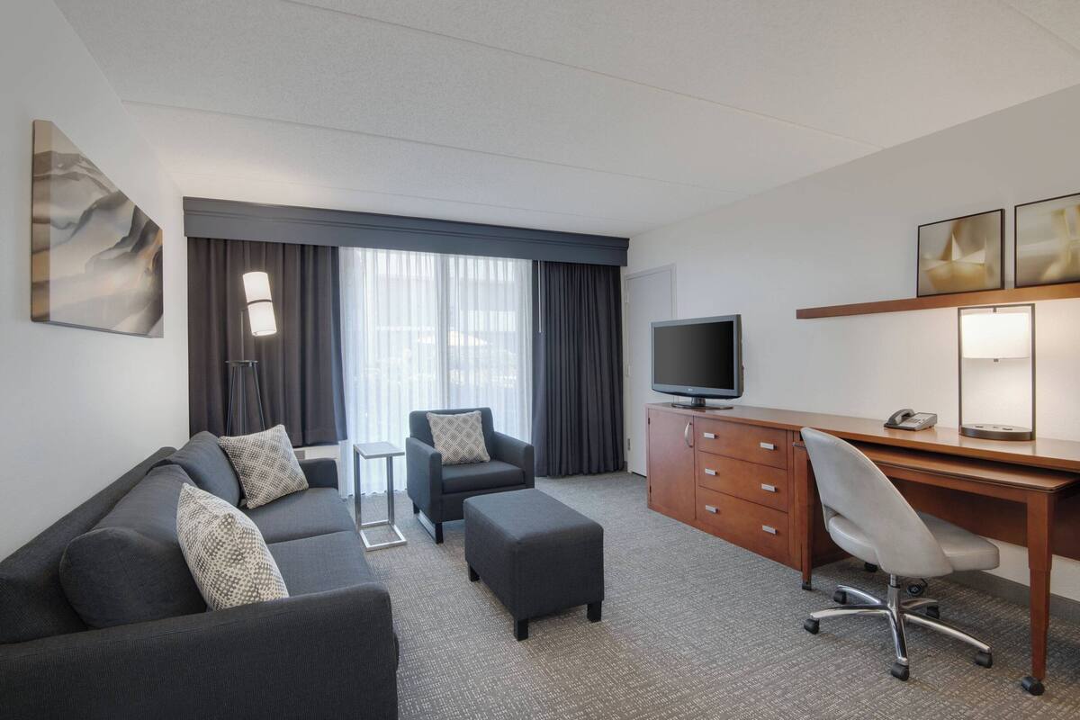 A hotel room with a sofa, a desk, a television, and a large window with curtains.