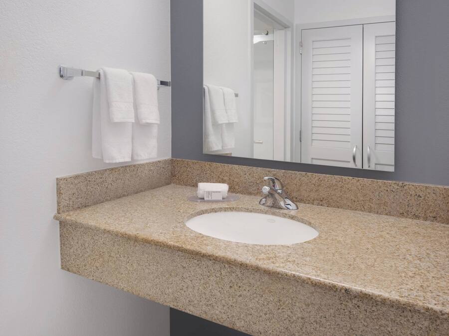 A bathroom with a granite countertop sink, a mirror, and two white towels hanging on a towel rack.