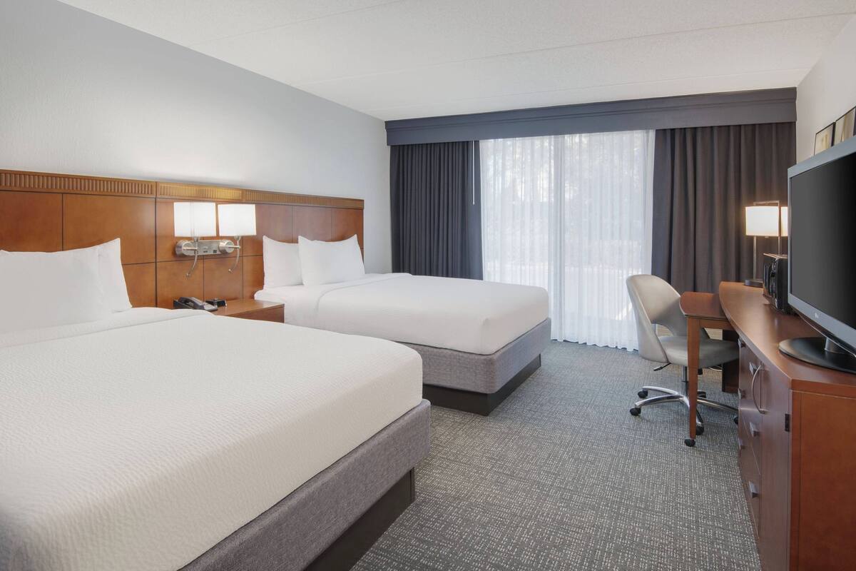 A hotel room with two beds, a desk, a chair, a television, and a window with curtains.