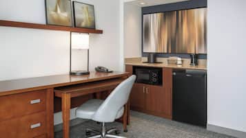 Ein Hotelzimmer mit einem Holztisch, einem grauen Bürostuhl, einer Mikrowelle, einer Kaffeemaschine und einer kleinen Küchenzeile.