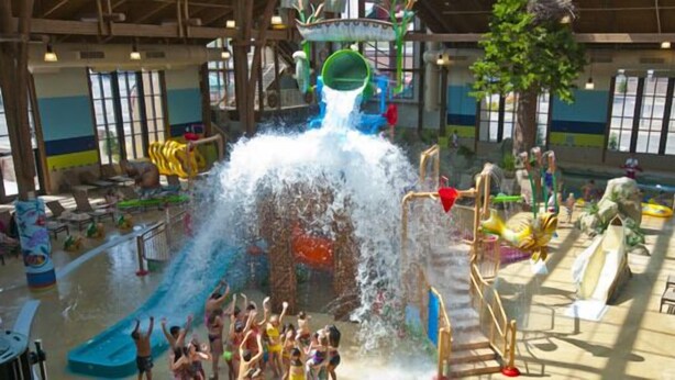 A water play area with slides and water jets, surrounded by seating and play structures. - Soaring Eagle Waterpark and Hotel (Mount Pleasant)