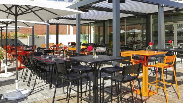 An outdoor dining area with tables and chairs, a covered seating area, and a building in the background. - ibis Styles Nancy Sud (Houdemont)