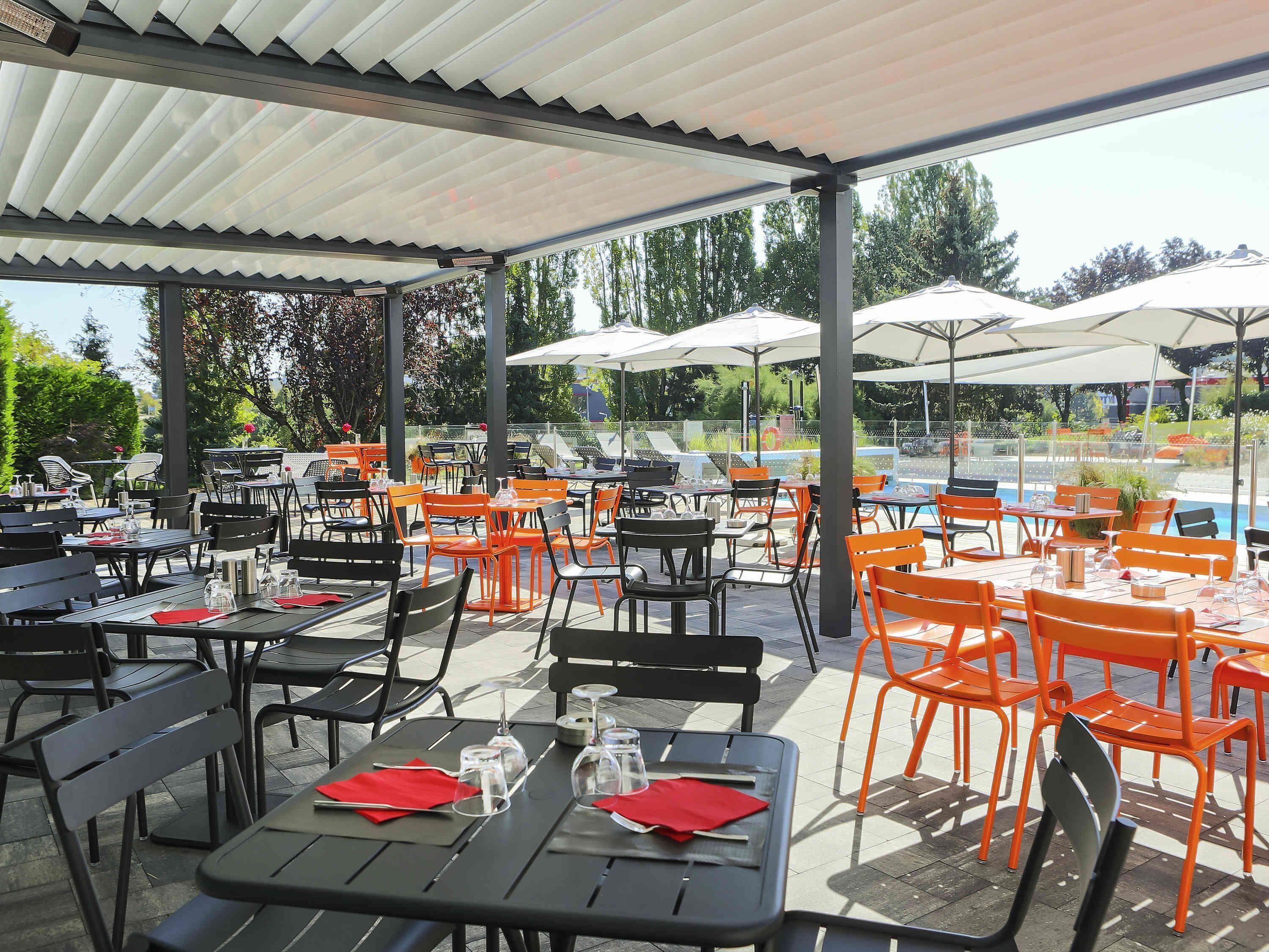 An outdoor dining area with tables and chairs, a pool, and a covered walkway.
