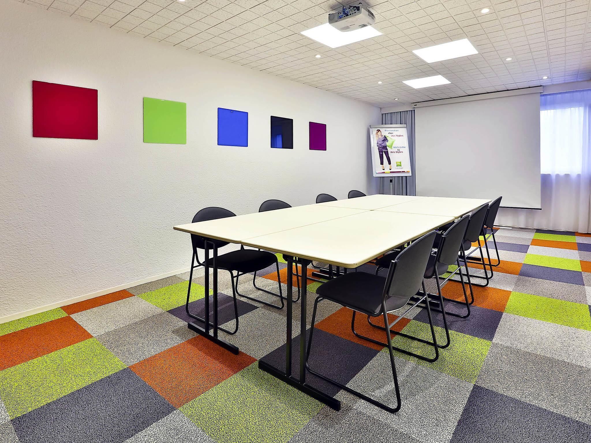 A conference room with a large table, chairs, a projector screen, and colorful wall decorations.