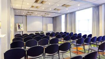 Una sala de conferències amb files de cadires, una pantalla de projector i un panell per a presentacions.