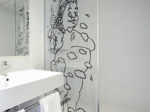 Une salle de bain avec un lavabo blanc, un miroir et un rideau de douche orné d’un motif floral noir.