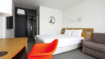 Ett hotellrum med en säng, ett skrivbord, en stol, en soffa, en spegel och ett konstverk som hänger på väggen.