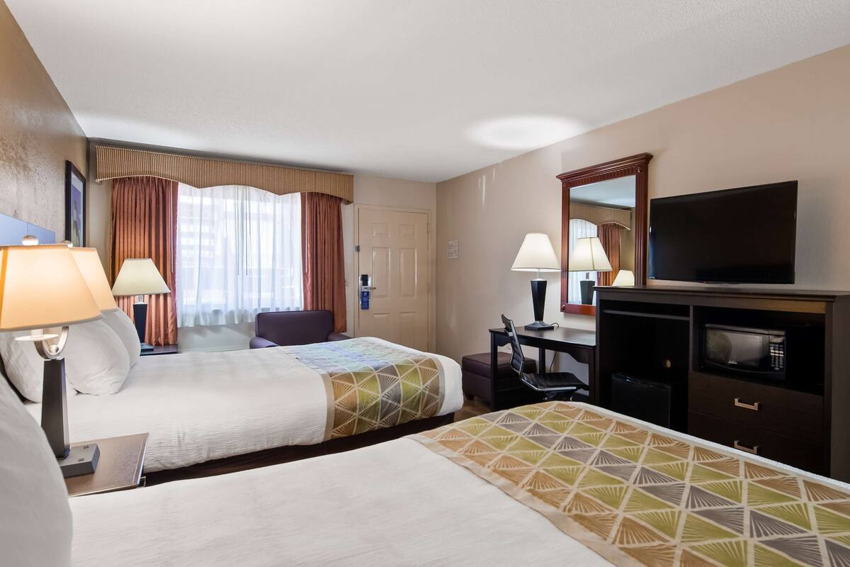 A hotel room with two beds, a desk, a television, and a microwave.