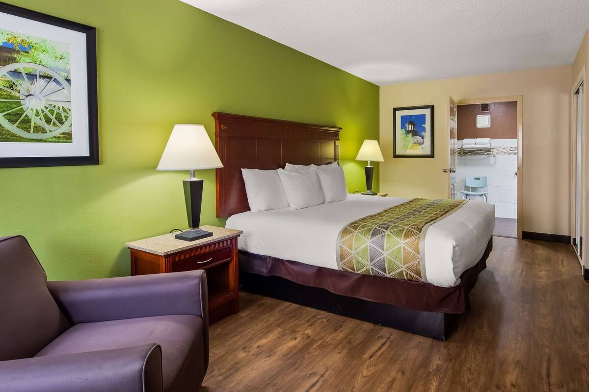 A hotel room with a bed, two bedside lamps, a chair, a desk, and a television.