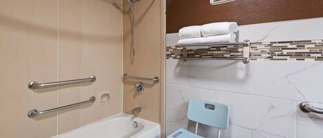 A bathroom with a bathtub, a shower with grab bars, a toilet with a raised seat, and a towel rack with folded towels.