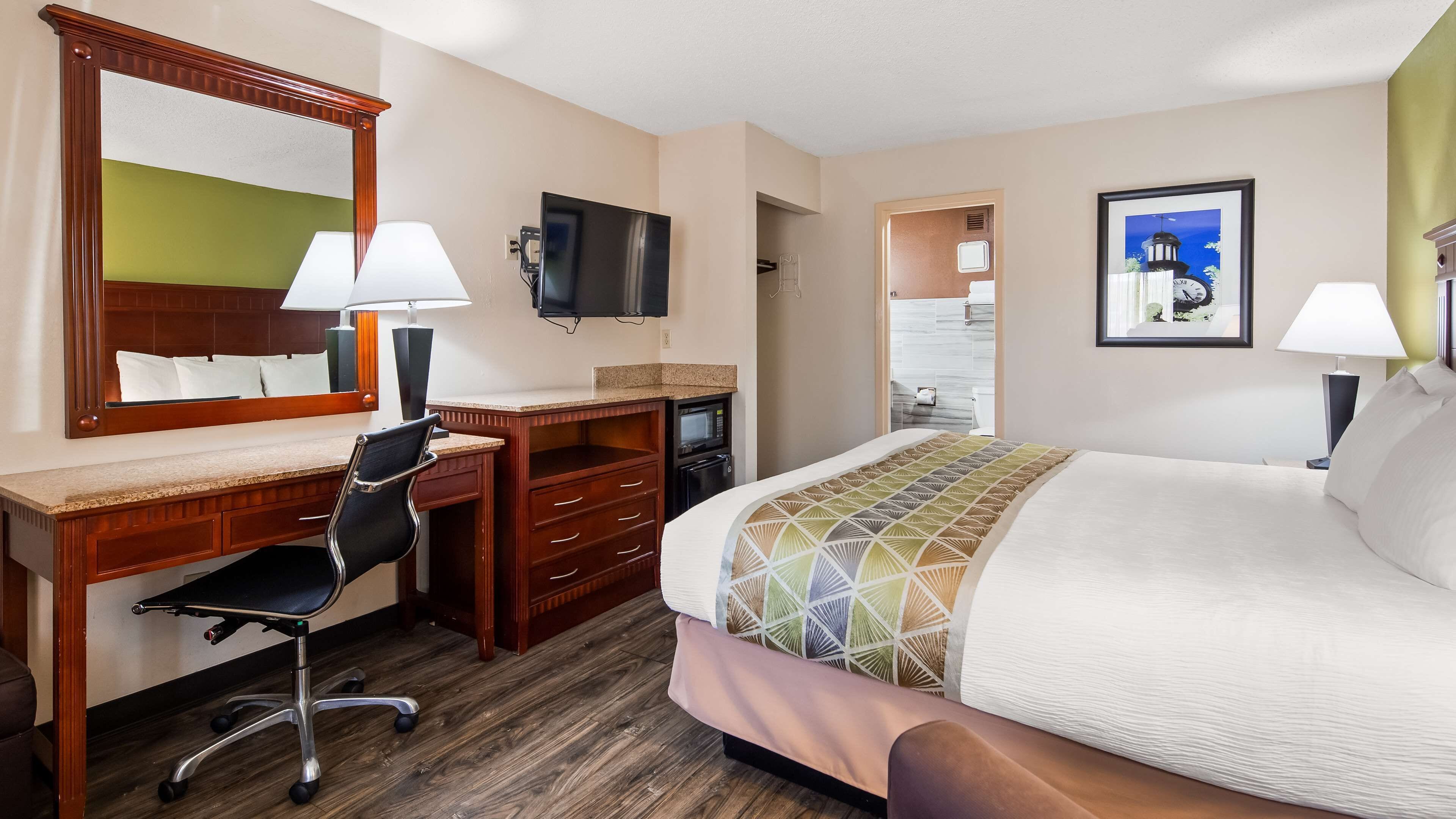 A hotel room with a bed, desk, chair, television, and a bathroom visible through an open door.
